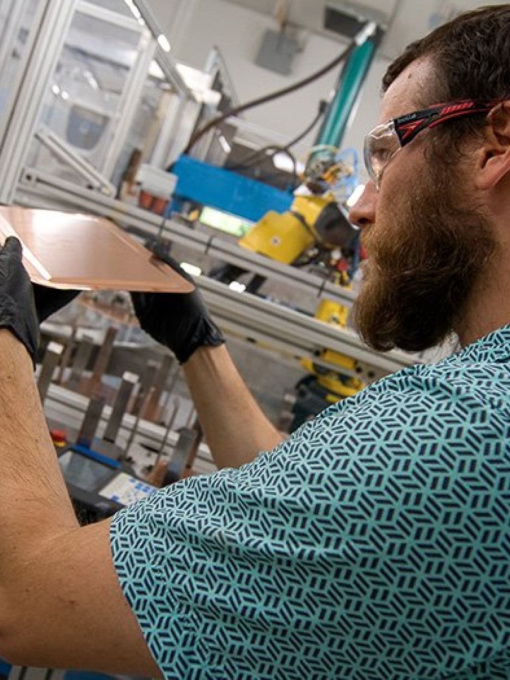 Personne manipulant une plaque métallique dans un environnement industriel équipé de machinerie.